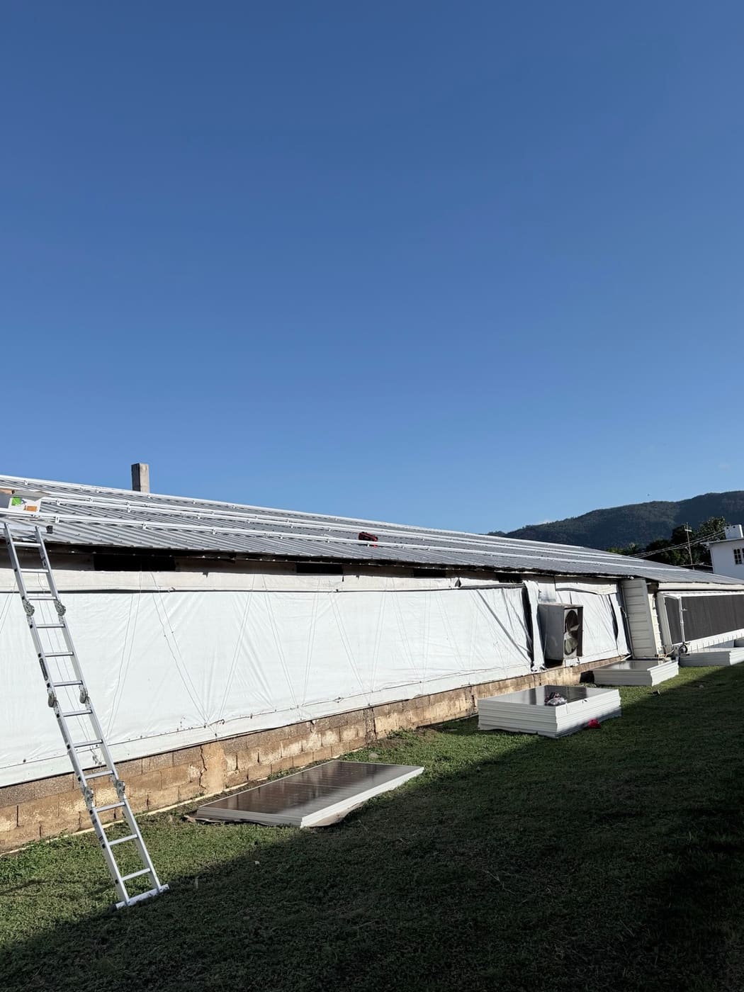The building mid-install, with mounting rails on the roof and panels stacked on the grass