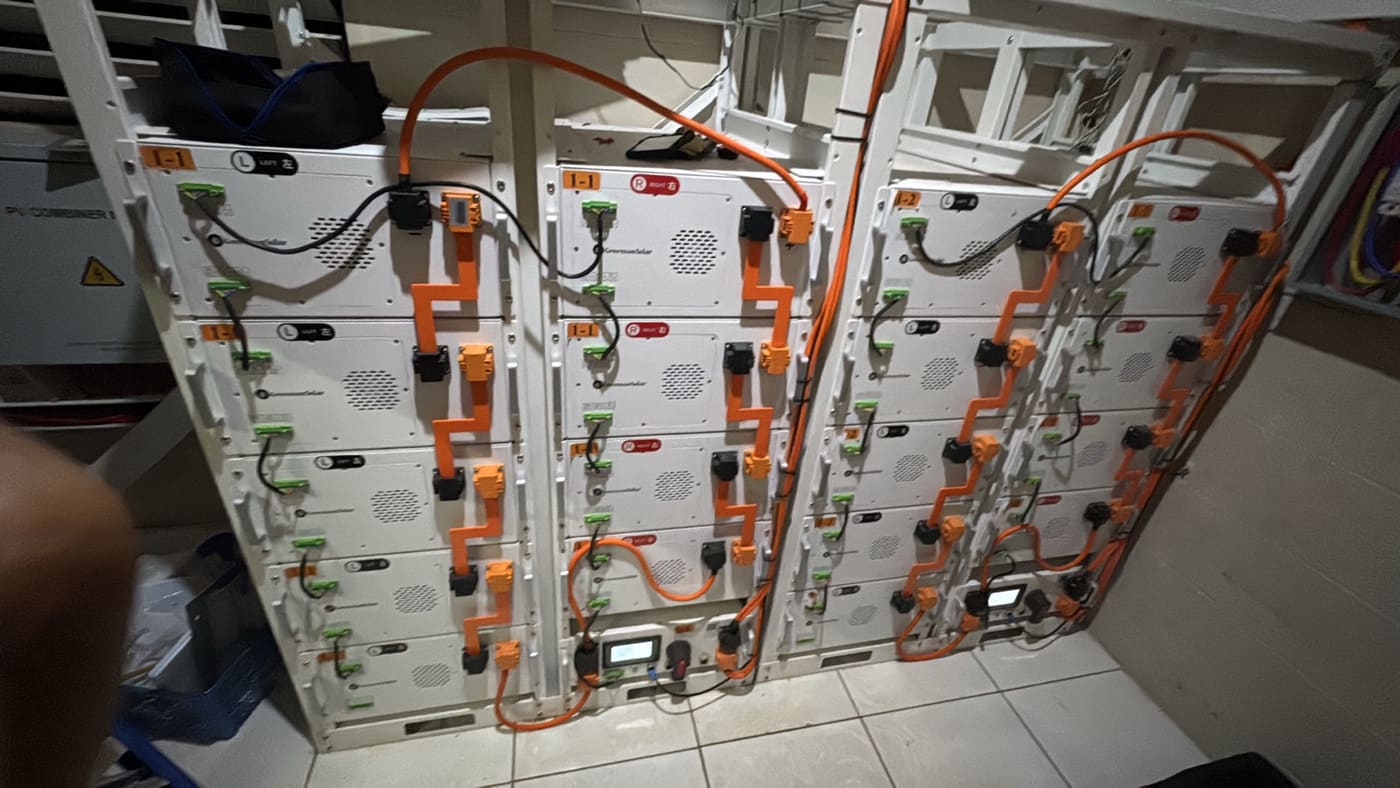 Stacked battery modules linked with orange busbars beside a PV combiner box