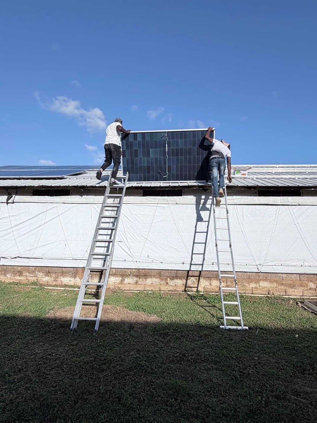Two installers carrying a large solar panel up onto a roof